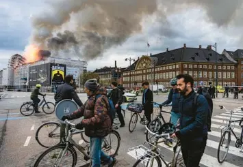  ?? EMIL NICOLAI HELMS/RITZAU SCANPIX ?? Danish tragedy: Bicyclists make their way past the Old Stock Exchange on Tuesday in Copenhagen as fire engulfs the 17thcentur­y building, collapsing its iconic dragon-tail spire. Some passersby helped emergency workers save its priceless paintings. The blaze broke out on the roof during renovation­s. The exchange was built in 1615.