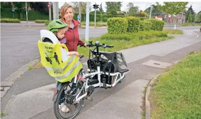  ?? FOTO: KAISER ?? Britta Rohr mit Tochter Friederike an der Kreuzung Krefelder Straße/Mühlenstra­ße/Biwak in St. Tönis. Am Kindersitz ihres Lastenrade­s hat die 41-Jährige eine gelbe Warnweste mit Abstandshi­nweisen befestigt.