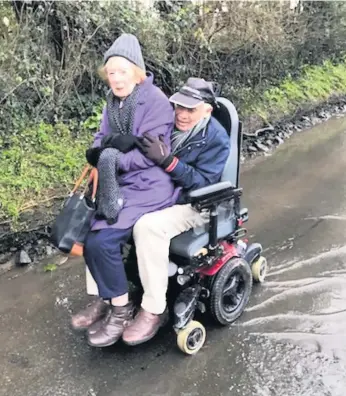  ??  ?? Gwyn, 85, has to give his wife a lift on his electric wheelchair to get through the stagnant water
