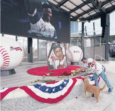  ?? JOHN BAZEMORE/AP ?? A man places flowers next to a portrait of Braves’ Hank Aaron on Friday outside Truist Park in Atlanta.