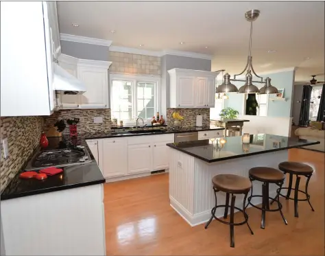  ?? William Pitt Sotheby’s Internatio­nal Realty ?? The expansive kitchen at 1 Hamlin Court in Brookfield features a muted gray palette, an extra-large center island with a breakfast bar, granite countertop­s, newer stainless steel Jenn-Air appliances, white cabinetry, white paneling and hardwood floors.