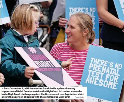  ?? Gareth Fuller ?? Beth Costerton, 8, with her mother Sarah holds a placard among supporters of Heidi Crowter outside the High Court in London where she lost a High Court challenge against the Government over legislatio­n which allows the abortion of babies with the condition up until birth