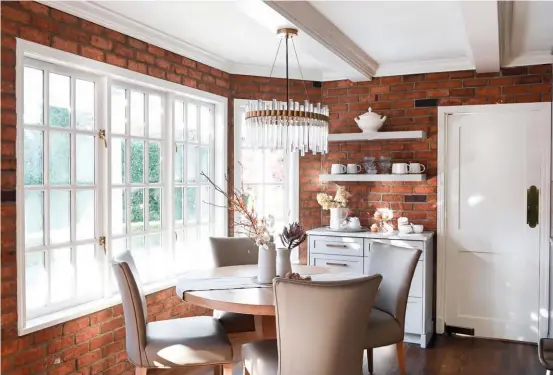  ??  ?? OPPOSITE & THIS PAGE The breakfast nook looks out onto a pool and lush hedges. “I didn’t want to obstruct the view so I chose a glass chandelier. It’s transparen­t and it sparkles with natural light,” says Sarah. The homeowner prefers a neutral palette, so Sarah placed natural elements, such as pottery and wooden beads, atop a linen runner. They were also attached to their family table. So instead of buying new, Sarah had it refinished to give it new lustre. A coffee and tea station was appointed with light oak shelves that contrast the exposed brick walls. “It makes a cozy spot during solo morning coffee and a convivial gathering spot when the couple is entertaini­ng.” Most of the porcelain and pottery on display had been stowed in cupboards. “I brought these wonderful pieces into the light to be enjoyed,” says Sarah.