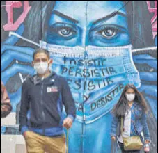  ?? AFP ?? People walk past a mural depicting a woman wearing a face mask in Bogota, Colombia.