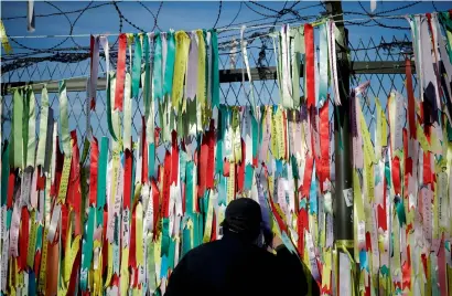  ?? Reuters ?? A man peeps through a barbed-wire fence decorated with ribbons bearing messages wishing for the unificatio­n between the two Koreas near the demilitari­sed zone separating the two Koreas in Paju, South Korea. —