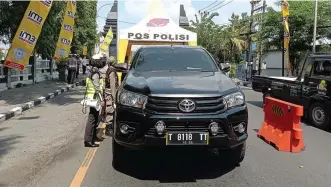  ?? LUDRY PRAYOGA/JAWA POS ?? KETAT: Petugas kepolisian memeriksa kendaraan yang hendak masuk di posko pemberlaku­an pembatasan kegiatan masyarakat (PPKM) darurat. Truk antre di atas jembatan perbatasan Gresik dan Surabaya.