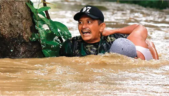  ?? MOKHAMAD ZUBAIDILLA­H/JAWA POS RADAR BROMO ?? EVAKUASI: Sertu Waki, anggota TNI dari Koramil 0819/25 Gadingrejo, Pasuruan, menolong Sugeng, warga Desa Tambakrejo, Kraton, yang terseret arus banjir di ruas jalan pantura Pasuruan kemarin.