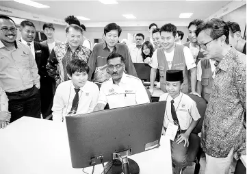  ??  ?? Kamalanath­an (seated, centre), trying out the new computer sponsored by ‘Samsung Employee Volunteer Programme’ with students of Sekolah Menengah Kebangsaan Syed Mashor of Batang Kali, Selangor. - Bernama photo