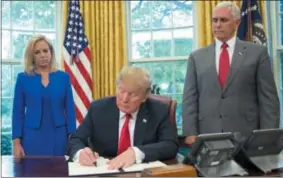  ?? THE ASSOCIATED PRESS ?? In the Oval Office of the White House on Wednesday, President Donald Trump signs an executive order to keep families together at the border. Standing behind Trump are Homeland Security Secretary Kirstjen Nielsen, left, and Vice President Mike Pence.