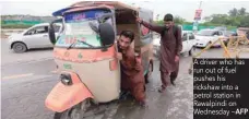  ?? AFP ?? A driver who has run out of fuel pushes his rickshaw into a petrol station in Rawalpindi on Wednesday —