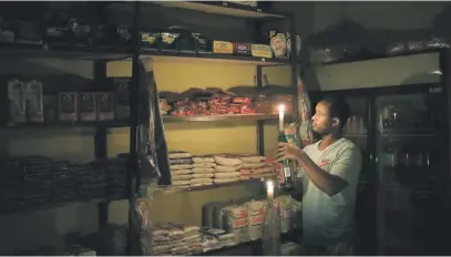  ?? Picture: Reuters ?? IN THE DARK. Mulugeta Desalegn, an owner of a spaza shop, picks an item for a customer as he holds a candle, in Senaone, Soweto, during load shedding in March.