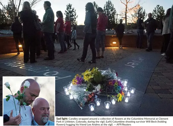  ?? — AFP/Reuters ?? Sad light: Candles wrapped around a collection of flowers at the Columbine Memorial at Clement Park in Littleton, Colorado, during the vigil. (Left) Columbine shooting survivor Will Beck (holding flowers) hugging his friend Lee Andres at the vigil.