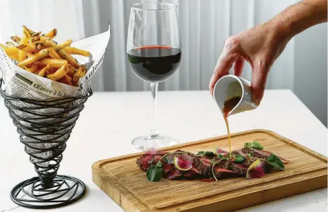  ?? Photos by Brett Coomer / Staff photograph­er ?? Steak frites, with a precise medium-rare center, has the intense flavor Texans love. Diners can dip thin-cut fries in a pitcher of beef juices.