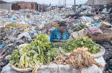  ?? RODRIGO ABD/AP ?? A woman selling greens waits for customers last week in the Croix des Bosalles market in Port-au-Prince, Haiti. The floor of the market is thick with decomposin­g trash and, in some places, small fires of burning trash.