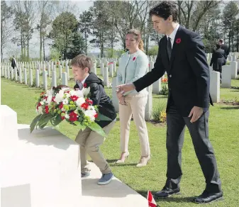  ?? CP ?? Under the watchful eyes of Sophie Grégoire Trudeau and Prime Minister Justin Trudeau, son Xavier places flowers at the cenotaph of the military cemetery in Bény-sur-Mer, France, on Monday.