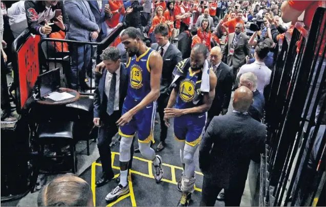  ??  ?? TRISTEZA. Kevin Durant se retira de la pista del Scotiabank Arena apoyado en un miembro del cuerpo médico de los Warriors y junto a su compañero Andre Iguodala.