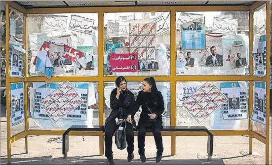  ?? BEHROUZ MEHRI / AFP ?? Jóvenes iraníes esperan el autobús en una parada empapelada con propaganda electoral en el centro de Teherán