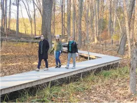 ??  ?? Eric Cavell and Anna Holland of Silver Spring and LouiseWhit­e of Annapolis stroll along the boardwalk on theWoodlan­d Trail at Glenstone.