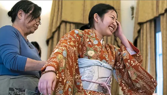  ?? Alexandra Wimley/Post-Gazette ?? Katsuko Shellhamme­r of Vandergrif­t, a volunteer from the Japan-America Society of Pittsburgh, helps student Asako Hirata of Hiroshima put on a kimono before participat­ing in a traditiona­l Japanese coming-of-age ceremony Friday at the University of Pittsburgh in Oakland.