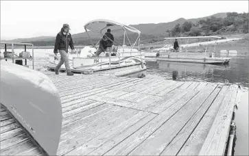  ?? Christina House For The Times ?? ZACH FOSS, left, helps tie up boats returning from fishing on Cachuma Lake. Many of the dusty hilltops that had emerged as Cachuma dropped to historic lows were once again submerged beneath the placid surface.