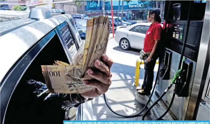  ?? — AFP ?? CARACAS: A customer shows Bolivar bills while at a gas station in Caracas where people queueing for petrol on Friday for the uncertaint­y about the price and availabili­ty of gasoline from Monday on, when the new currency with five fewer zeros starts circulatin­g in Venezuela.