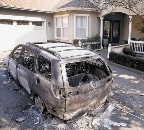  ??  ?? A home on Skyfarm Drive in Santa Rosa appears to be undamaged by Monday's firestorm, although it was different story for a burned-out minivan parked in the driveway.