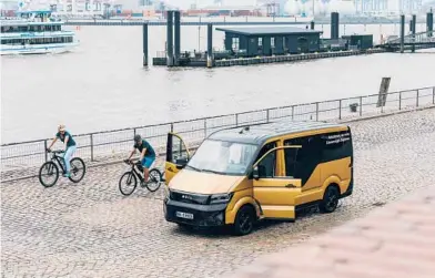  ?? FELIX SCHMITT/THE NEW YORK TIMES ?? Cyclists check out at a parked electric van operated by a VW subsidiary June 30 in Hamburg, Germany. The vehicles steer themselves, but technician­s at a remote control center keep an eye on their progress with the help of video monitors.