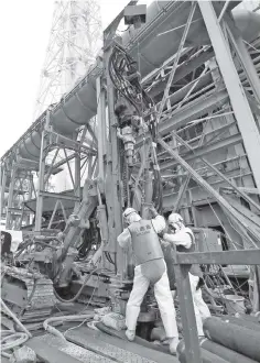  ??  ?? Workers wearing protective clothes and masks unveil constructi­on material for building an undergroun­d frozen wall at the No. 4 reactor at Tokyo Electric Power Co.’s Fukushima Dai-ichi nuclear power plant in Okuma.