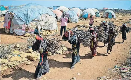  ?? TONY KARUMBA / AFP ?? Mujeres cargando leña en un campo de desplazado­s de Somalia, uno de los países azotados por el hambre