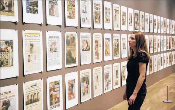  ?? PHOTOS BY MATT DUNHAM/AP PHOTO ?? A staff member poses for photograph­s looking at German visual artist Hans-Peter Feldmann’s installati­on “9/12 Frontpage” during the media preview for the “Age of Terror: Art since 9/11” exhibition at the Imperial War Museum in London.