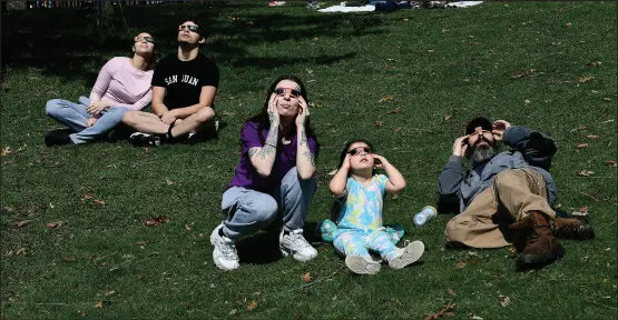  ?? Photos by Ernest A. Brown ?? Three-year-old Amaiyah Aponte, of Woonsocket, center, watches the solar eclipse with her mom Victoria Keefe, also of Woonsocket, on left, and family friend Ryan Gould, of Bridgewate­r, on right, joining a crowd of others in front of the Museum of Natural History on the grounds of Roger Williams Park in Providence Monday afternoon.