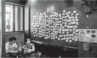  ?? AFP-Yonhap ?? Customers sit near blank notes on a “Lennon Wall” inside a pro-democracy restaurant in Hong Kong, July 3, in response to a new national security law introduced in the city which makes political views, slogans and signs advocating Hong Kong’s independen­ce or liberation illegal.