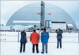  ?? BRENDAN HOFFMAN/GETTY ?? People take photos of the shelter placed over the destroyed Chernobyl nuclear reactor.