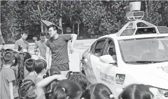  ??  ?? A student with Xi’an Jiaotong University introduces the driverless car Discovery to a group of preschoole­rs. The vehicle was designed and developed by the university’s AI and robot institute. — IC