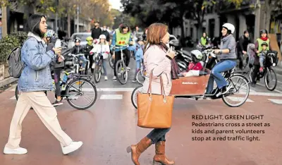  ?? ?? RED LIGHT, GREEN LIGHT Pedestrian­s cross a street as kids and parent volunteers stop at a red traffic light.