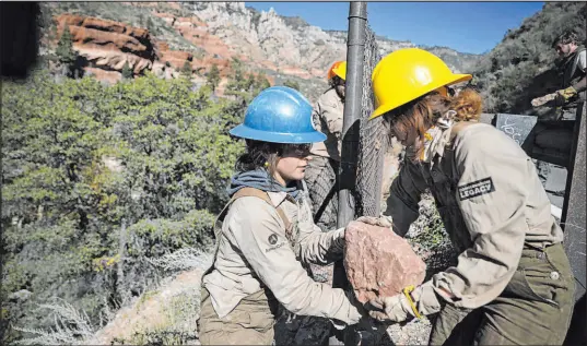  ?? Jake Bacon The Associated Press ?? Crew leader Hannah Green, left, takes a boulder from crew member Kendel Godfrey as the two work to block holes in a fence along Highway 89A in Oak Creek Canyon, near Sedona, Ariz., on Oct. 20. The area’s fragile ecosystem has been hit hard by visitors.