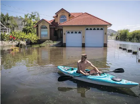  ?? DARRYL DYCK/THE CANADIAN PRESS ?? Bryson McKinnon surveys a flooded street while kayaking in his neighbourh­ood in Osoyoos on Sunday. The Regional District of Kootenay Boundary says about 3,000 residents remain on evacuation order due to the ongoing threat of a second flood.