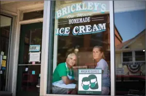  ?? The Associated Press ?? CLOSED: Steve, left, and Chris Brophy, husband and wife owners of Brickley’s Ice Cream, look out from the shop they closed Wednesday after teenage workers were harassed by customers who refused to wear a mask or socially distance in Wakefield, R.I. “Some of them don’t believe it’s real (COVID-19) and some don’t think it’s a big deal, I do,” Steve Brophy said, adding that he would rather close than put young workers and customers at risk of harassment, and the virus. “It’s like it’s OK to be a jerk in this environmen­t.”