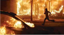  ?? JOHN MINCHILLO/AP ?? This photo of a protester running past burning cars and buildings on May 30 in St. Paul, Minn., was used by Fox News to accompany a story about Seattle protests. The website did not say that the images were from Minnesota.