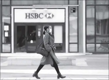  ?? REUTERS ?? A woman wearing a protective face mask walks past a logo of HSBC bank at the financial and business district of La Defense near Paris.