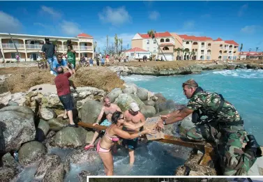  ?? AP PHOTOS ?? RECOVERY: A human chain, above, passes supplies provided by a Dutch soldier after the passing of Hurricane Irma in St. Maarten Friday. At right, floodwater­s surround Gilbert’s Resort in Key Largo, Fla.