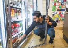  ?? Gabrielle Lurie / The Chronicle ?? 7-Eleven employee Rajan Bhatti checks the supply in the soda case at a store on Mission Street in San Francisco.