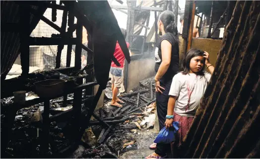  ?? (SUN.STAR FOTO/ARNI ACLAO) ?? A BLEAK SEASON. Residents examine the ruins of their houses in Barangay Apas, Cebu City, after a fire yesterday afternoon struck a sitio near Archbishop Reyes Ave.