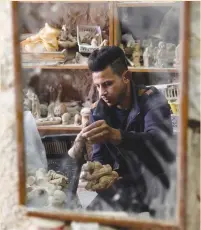  ?? (Raneen Sawafta/Reuters) ?? A PALESTINIA­N MAN’s image is reflected in a mirror as he collects figurines for sale at a workshop in Bethlehem on Monday.