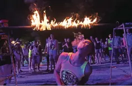  ??  ?? A partygoer lighting a cigarette on a fiery limbo stick during a Full Moon Party.