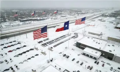  ?? Photograph: John Moore/Getty Images ?? Flags fly over car dealership­s as light traffic moves through snow and ice on US Route 183 on Thursday in Irving, Texas.