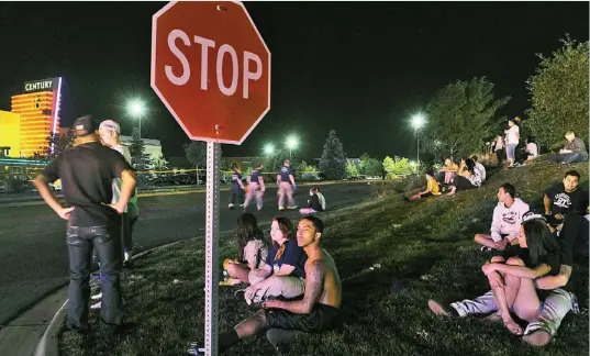  ??  ?? Shocked: Anxious moviegoers sit on a grassy slope opposite the mall after police sealed it off in the hunt for the gunman