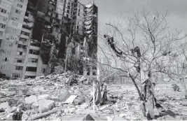  ?? EFREM LUKATSKY AP ?? A resident sifts through clothes and other debris that litter the grounds next to a ruined building after it bombed by Russian in Kharkiv, Ukraine.