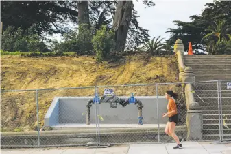  ??  ?? A woman runs along Hayes Street next to fencing alongside Alamo Square Park, a popular destinatio­n that is blocked off while waiting for its new sod, shrubs and spring flowers.