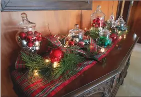  ??  ?? A plaid table runner covers an antique buffet. A collection of apothecary jars are filled or partially filled with colorful balls in various color combinatio­ns. Lights make the glass sparkle and plaid ribbon ties in the runner. This also would work...